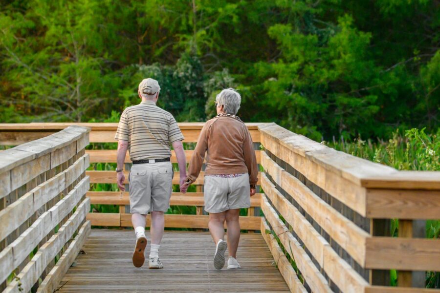 Senior pair walking on a wooden bridge, sharing a moment in a peaceful outdoor setting.