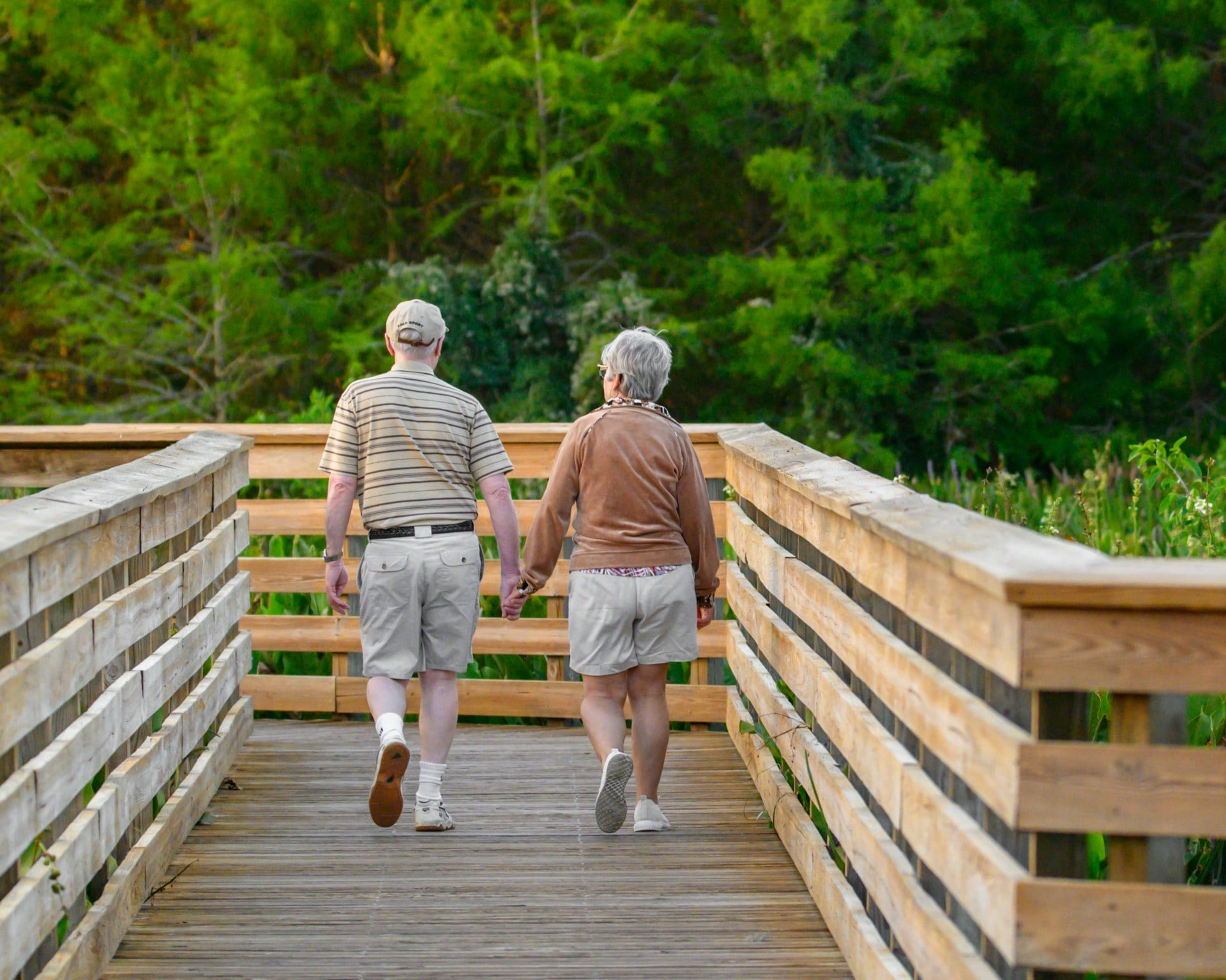 Senior pair walking on a wooden bridge, sharing a moment in a peaceful outdoor setting.