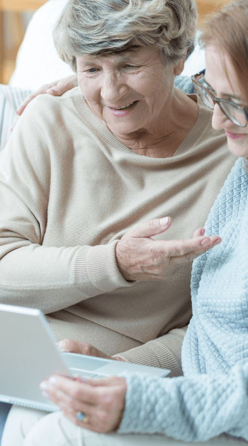 Older woman receiving guidance on a laptop from another woman, both smiling.