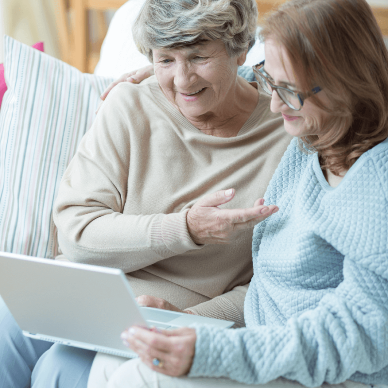 Older woman receiving guidance on a laptop from another woman, both smiling.