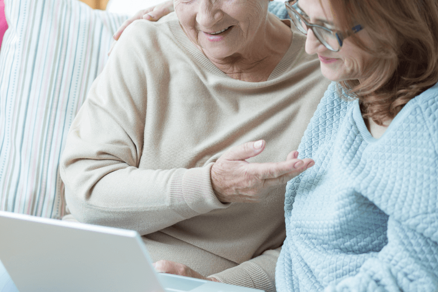 Older woman receiving guidance on a laptop from another woman, both smiling.