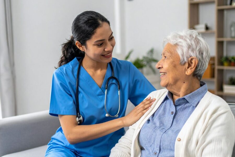 Professional in-home caregiver supporting a senior woman during post-surgery recovery at home.