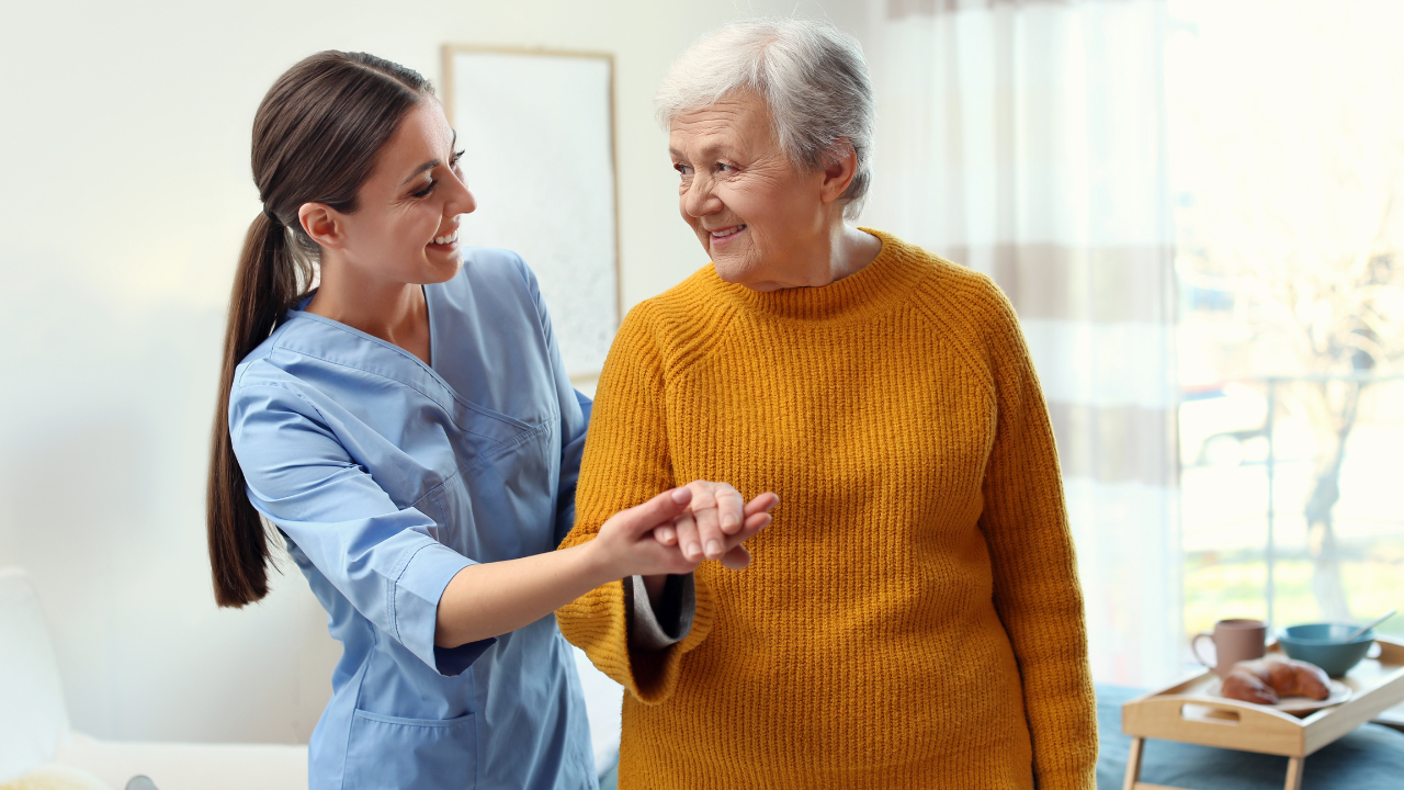 A caregiver gently supports a smiling senior woman as they walk together at home.