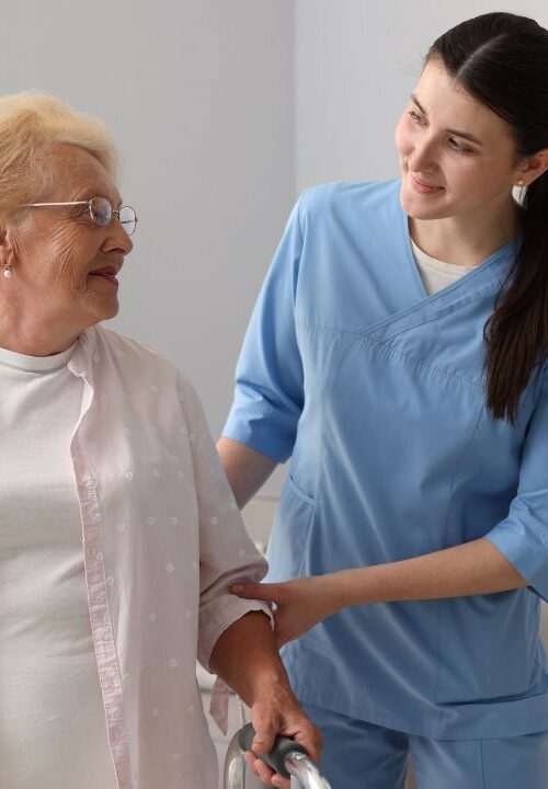 Caregiver assisting an older adult using a walker during in-home care.