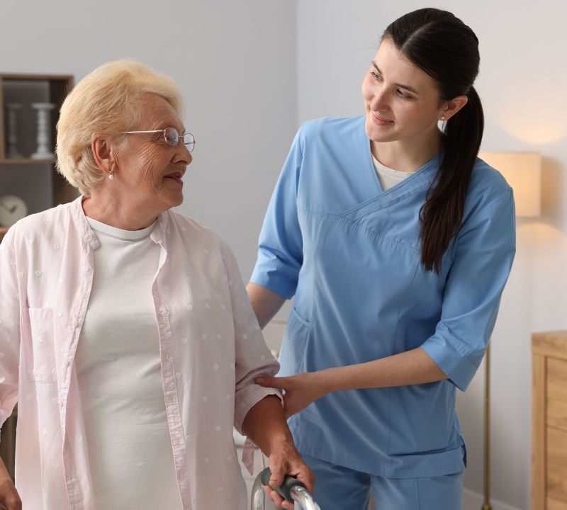 Caregiver assisting an older adult using a walker during in-home care.