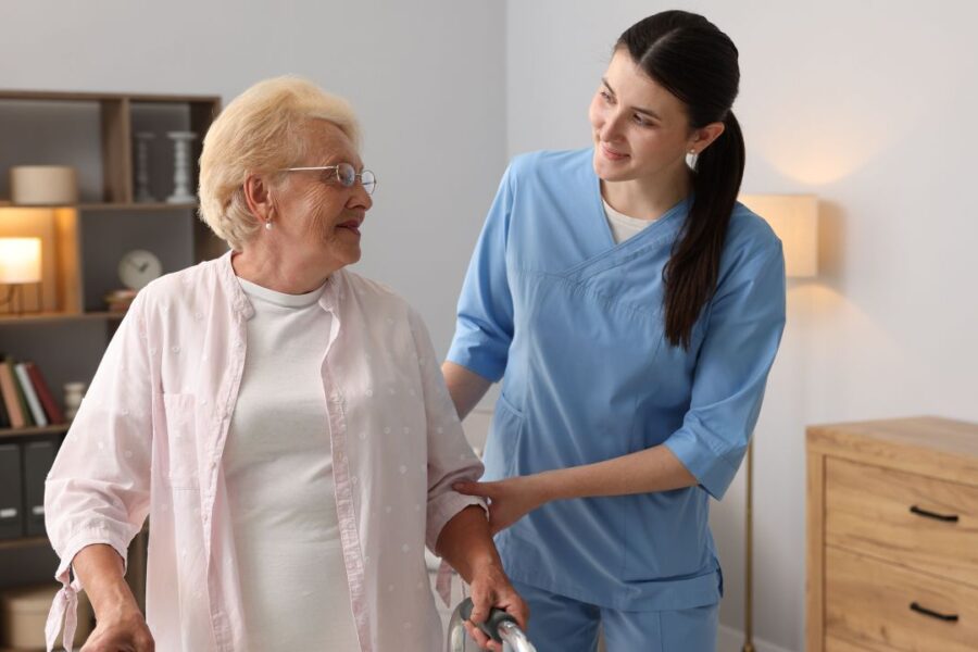 Caregiver assisting an older adult using a walker during in-home care.