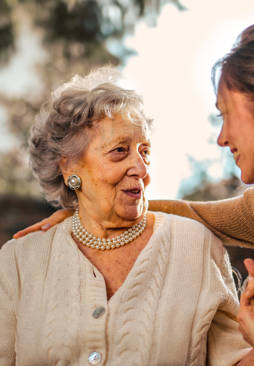 Adult daughter holding hands and talking with her mother outdoors.