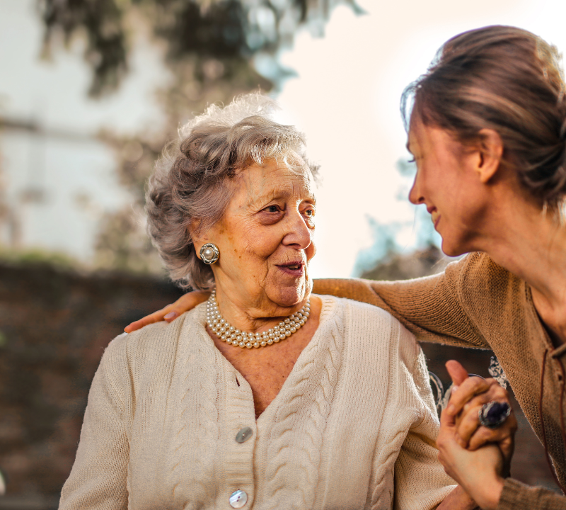 Adult daughter holding hands and talking with her mother outdoors.