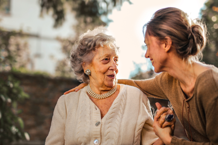 Adult daughter holding hands and talking with her mother outdoors.