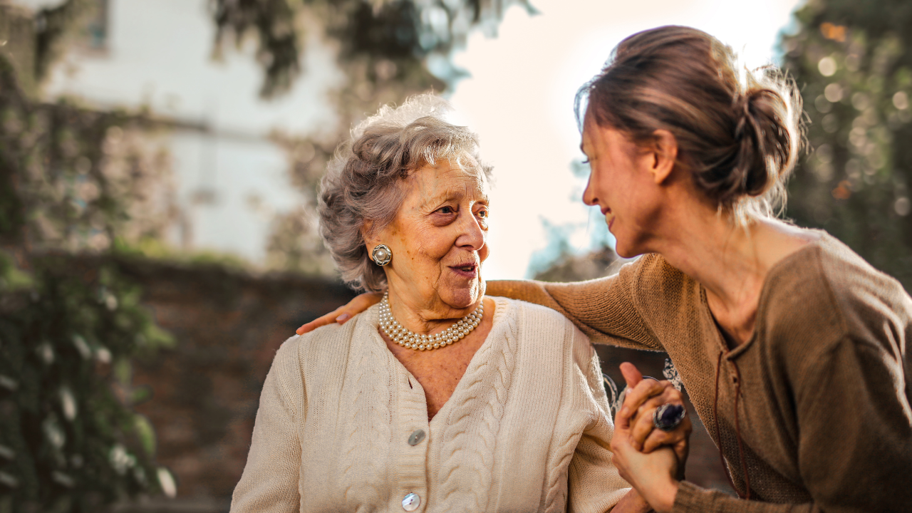 Adult daughter holding hands and talking with her mother outdoors.