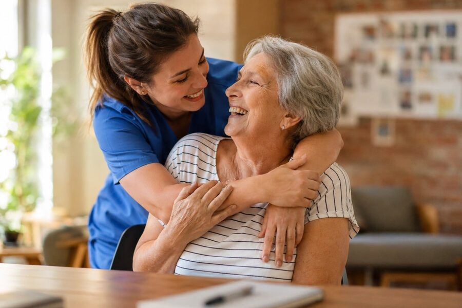 A younger woman hugs an older woman in her home, highlighting a moment of connection and compassion.